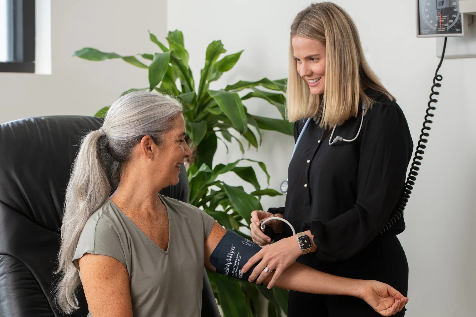 Nurse taking accurate blood pressure readings of smiling female patient in a clinical setting